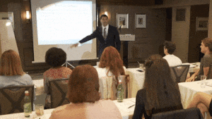 chiropractor hypnotherapist Dr. Theo Kousouli in a suit teaching corporate seminars and Be A Master seminar classes to students.